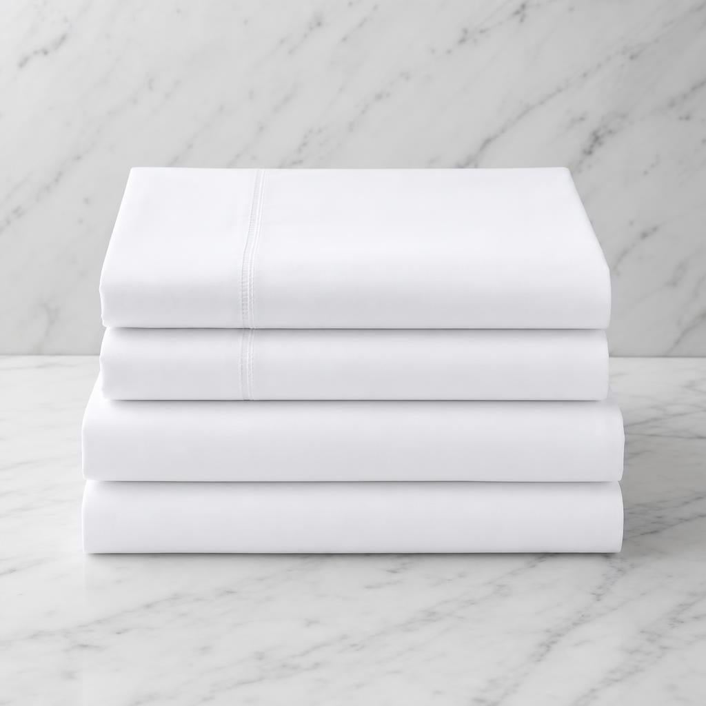 Squared stack of bright white percale hotel bed linens on soft white marble